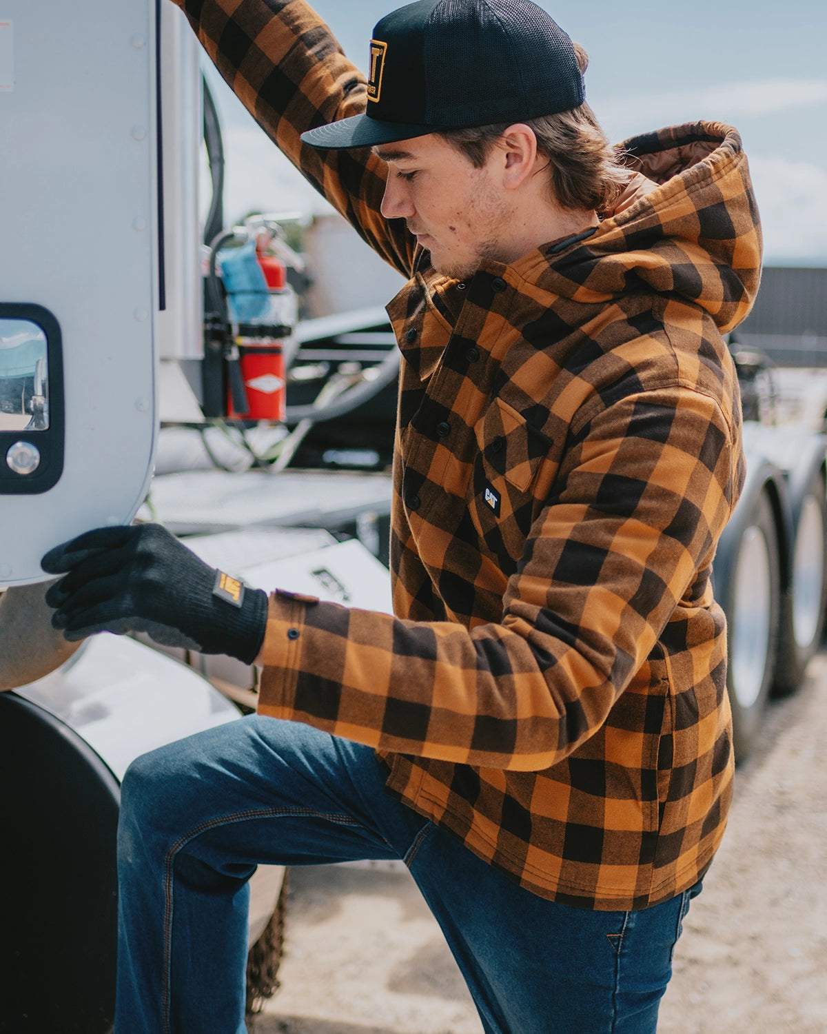 CAT workwear men's hooded flannel shirt jack bronze on model climbing into a tractor trailer