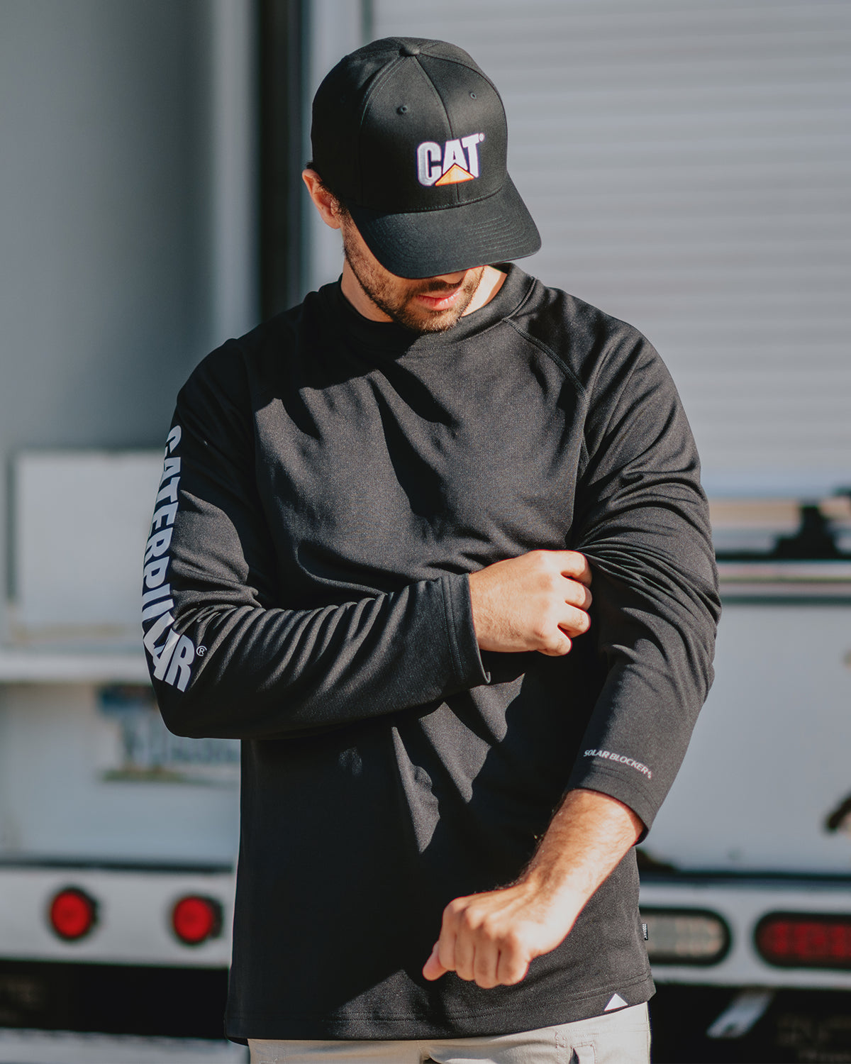 CAT Workwear Men's Lightweight Cooling Long Sleeve Crew Tee Black In Front Of Truck Adjusting Sleeve