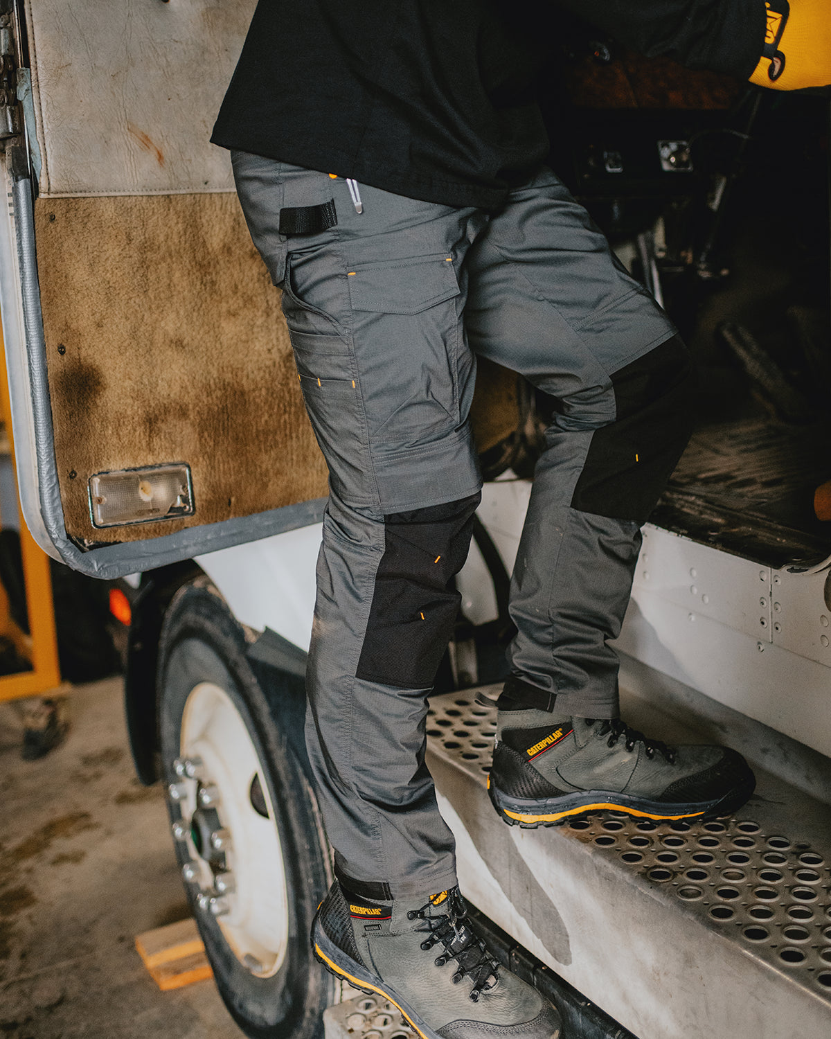 Cat workwear Men's Nexus Work Pant Dark Shadow. Person wearing gray work pants and black shoes stepping onto a vehicle.